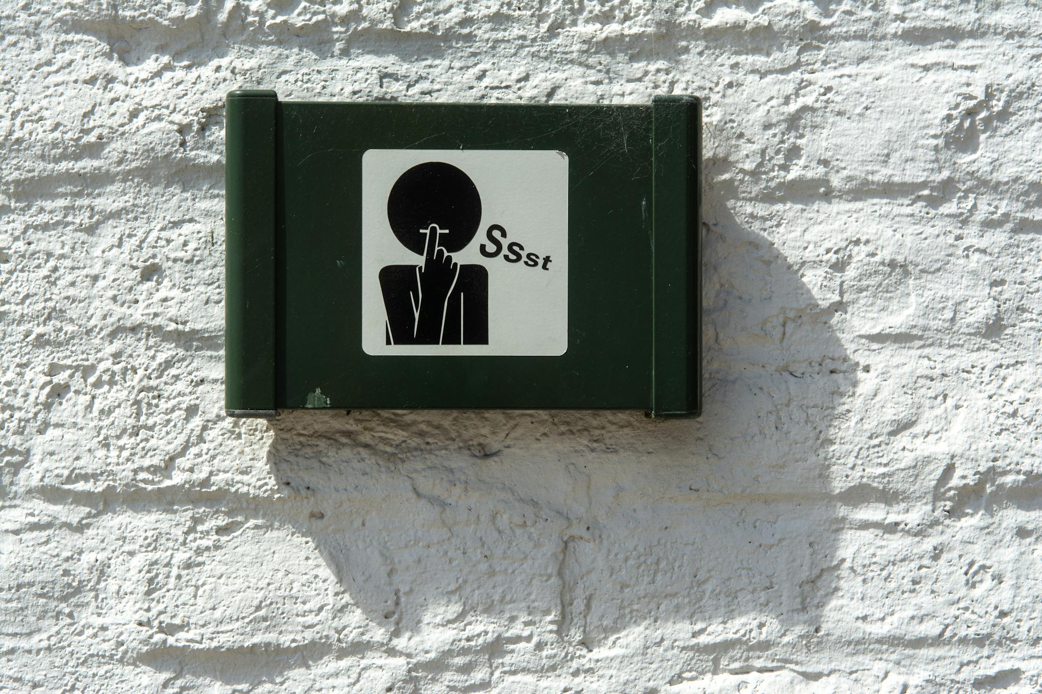 A green sign on a white brick wall indicating silence with a 'Ssst' symbol.